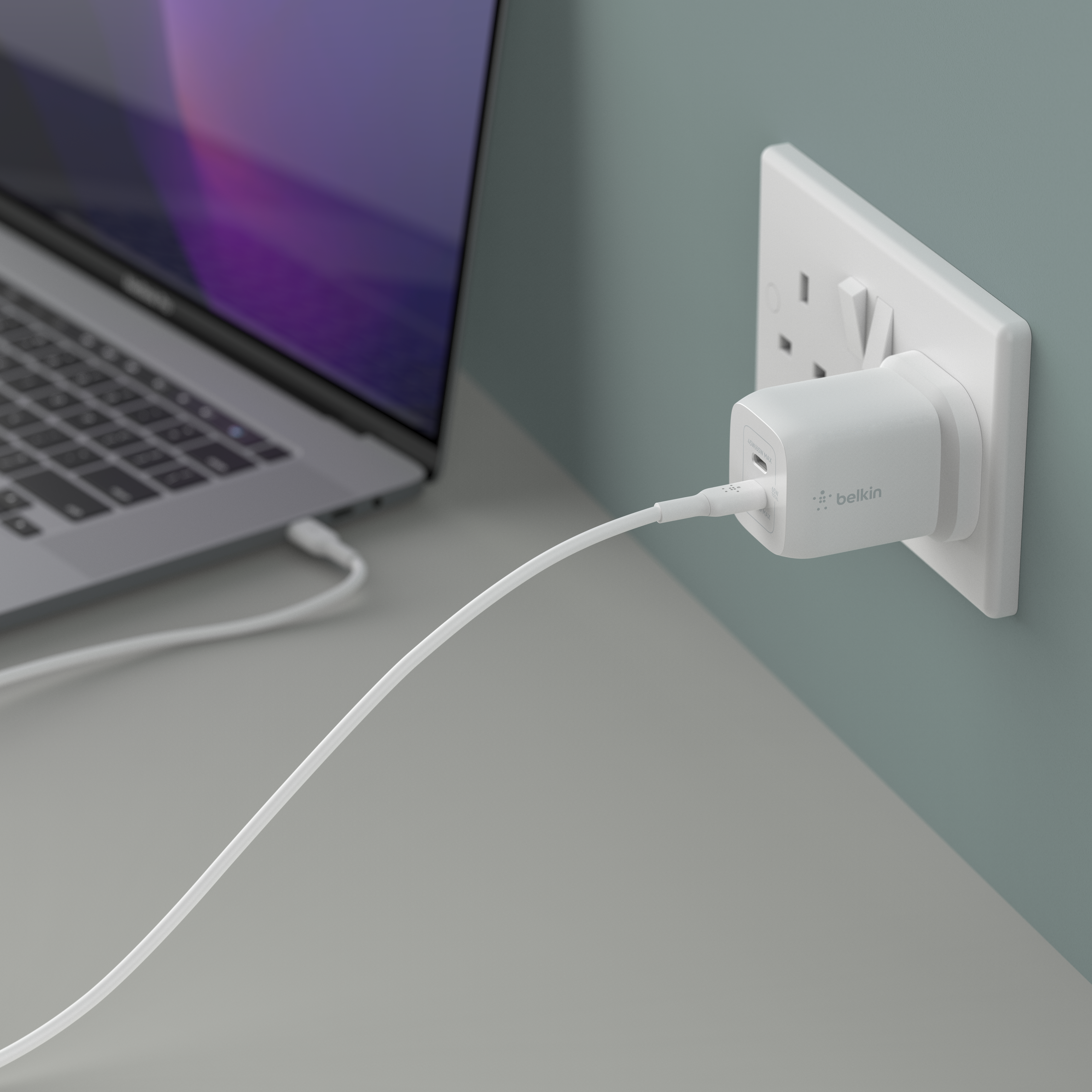 An image of a Belkin Dual USB-C&reg; GaN Wall Charger with PPS 65W in use, plugged into a wall outlet with USB-C cable plugged into bottom port. 